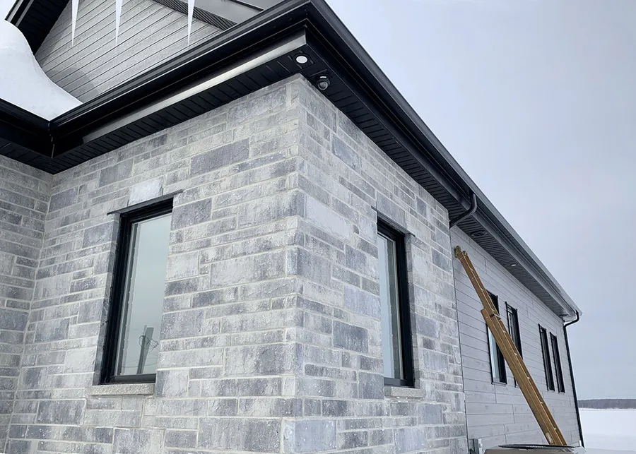 Gouttières noires sans joint posées sur une résidence en pierre grise à Terrebonne