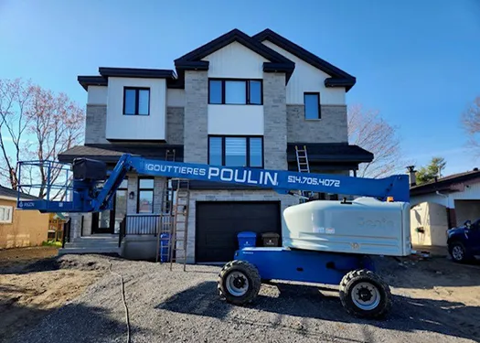Nacelle de chantier devant une maison à deux étages avec gouttières neuves